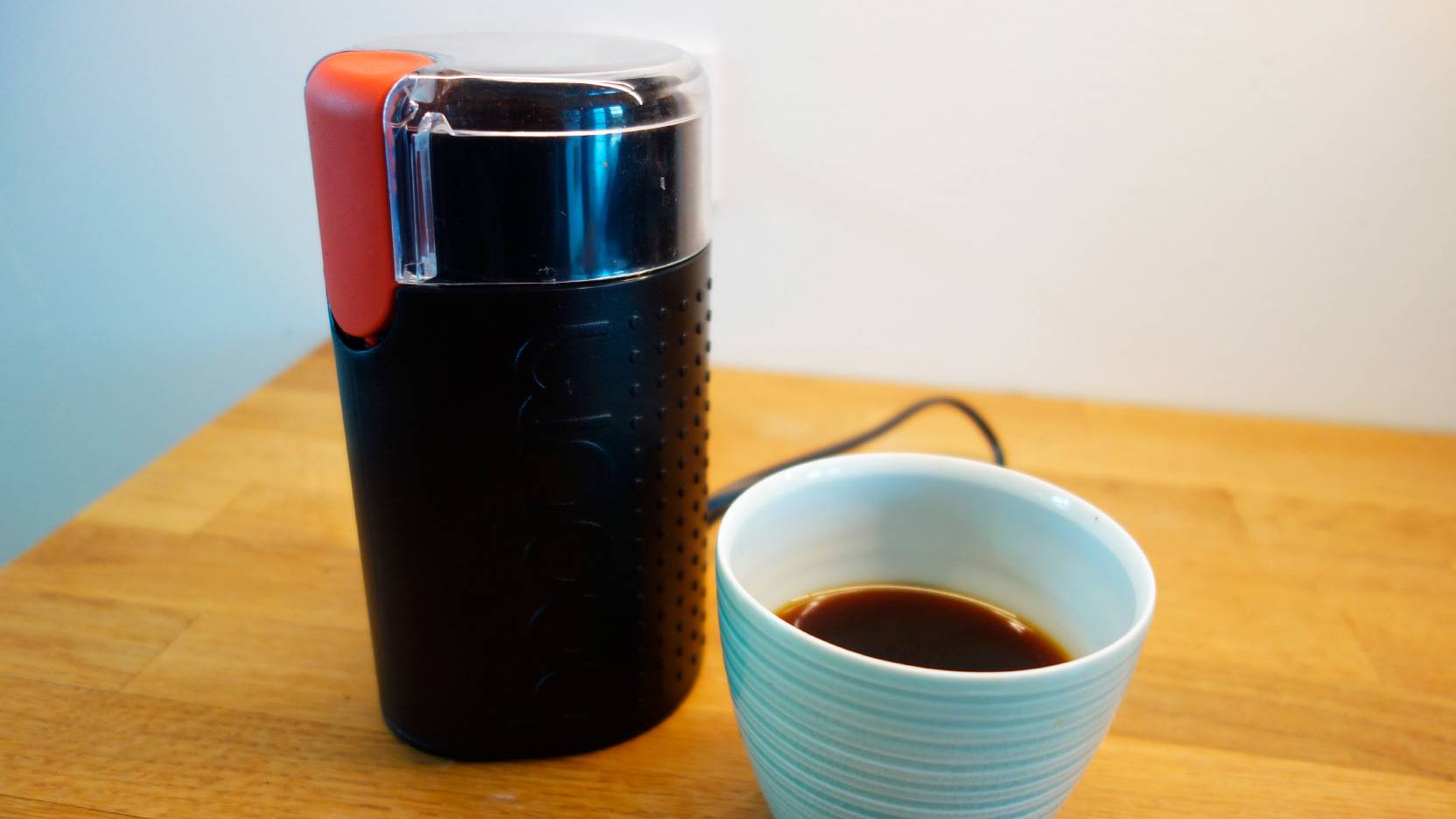 Billede af den sorte kaffemølle Bodum Bistro ved siden af en friskbrygget kop kaffe