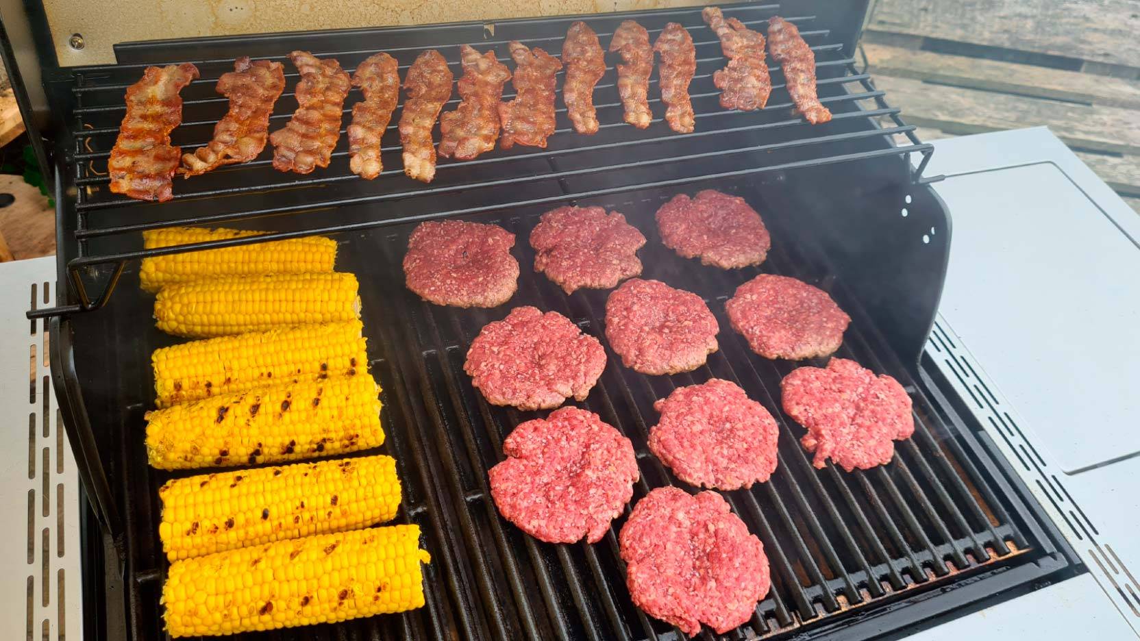 Billede af grillarealet på Charbroil Professional Pro S3 med burgerbøffer, majs og bacon
